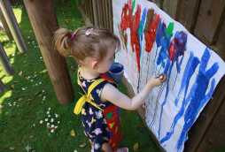 children's nursery facilities, little girl painting paper on fence outside multi-colours
